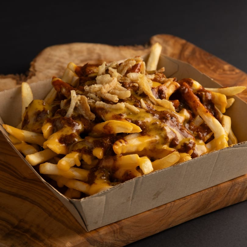 Dogs & Deli chili cheese fries with crispy onions in a cardboard tray on a wooden board.