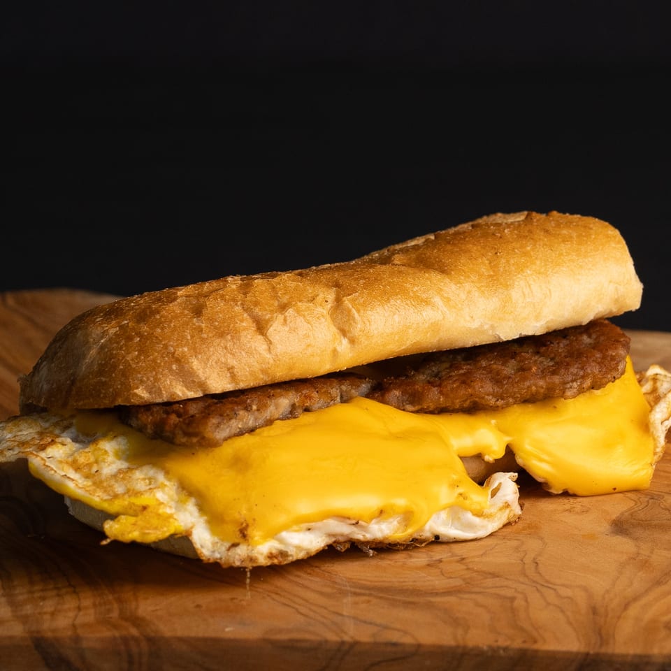 A Dogs & Deli hot dog with sausage, melted cheese, and fried egg on a bun.