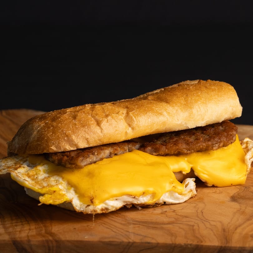 A Dogs & Deli hot dog with sausage, melted cheese, and fried egg on a bun.